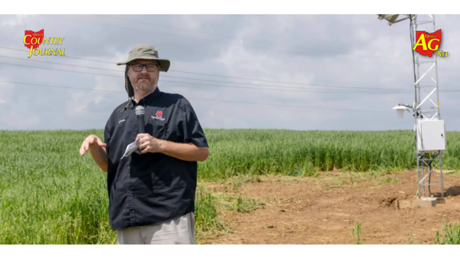 Speaker in an OSU Extension shirt addresses a field crowd beside a mesonet weather station in a grain field.